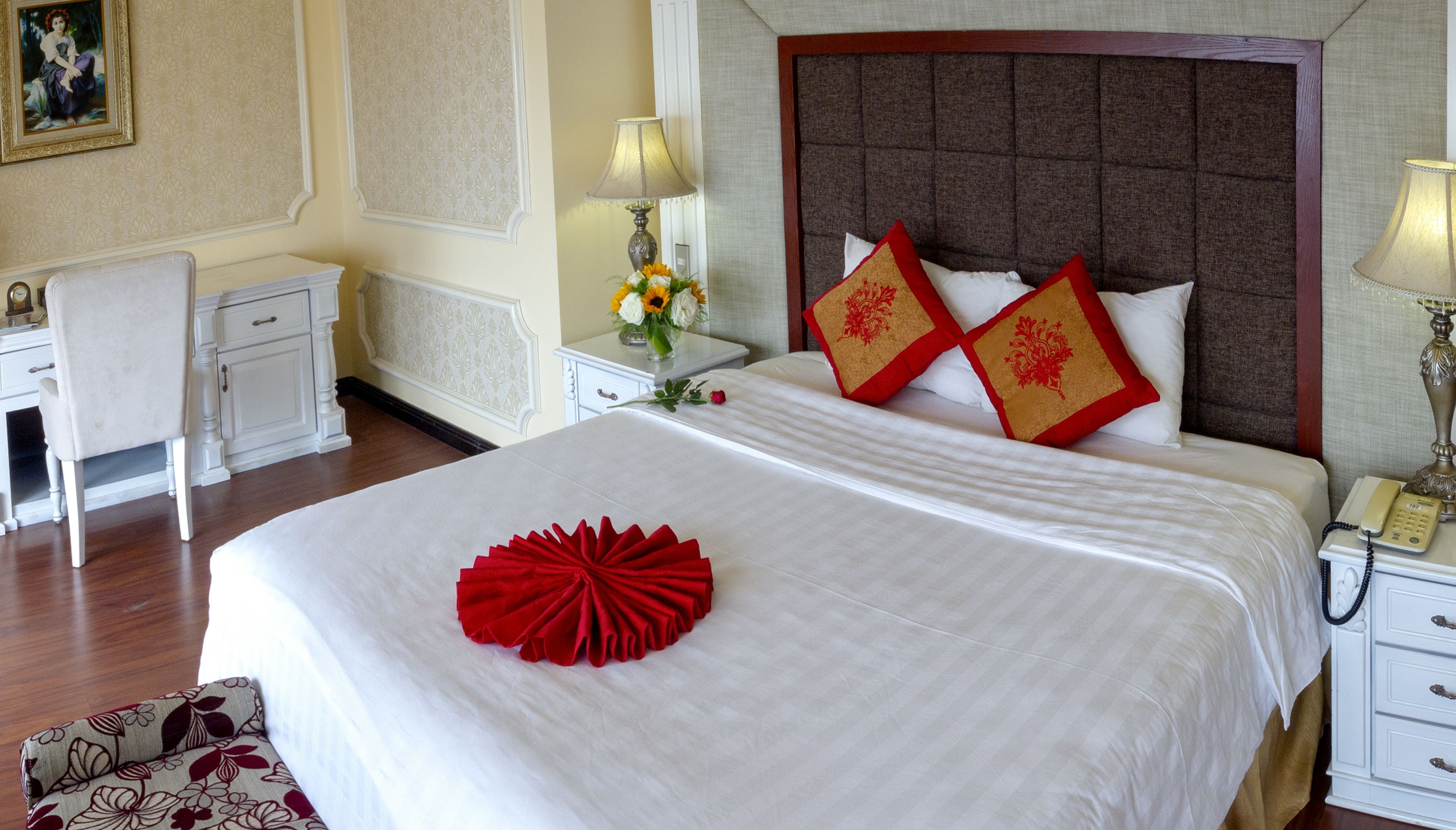 A neatly arranged hotel room with a large bed, a bedside table with a lamp, a chair, and a desk.