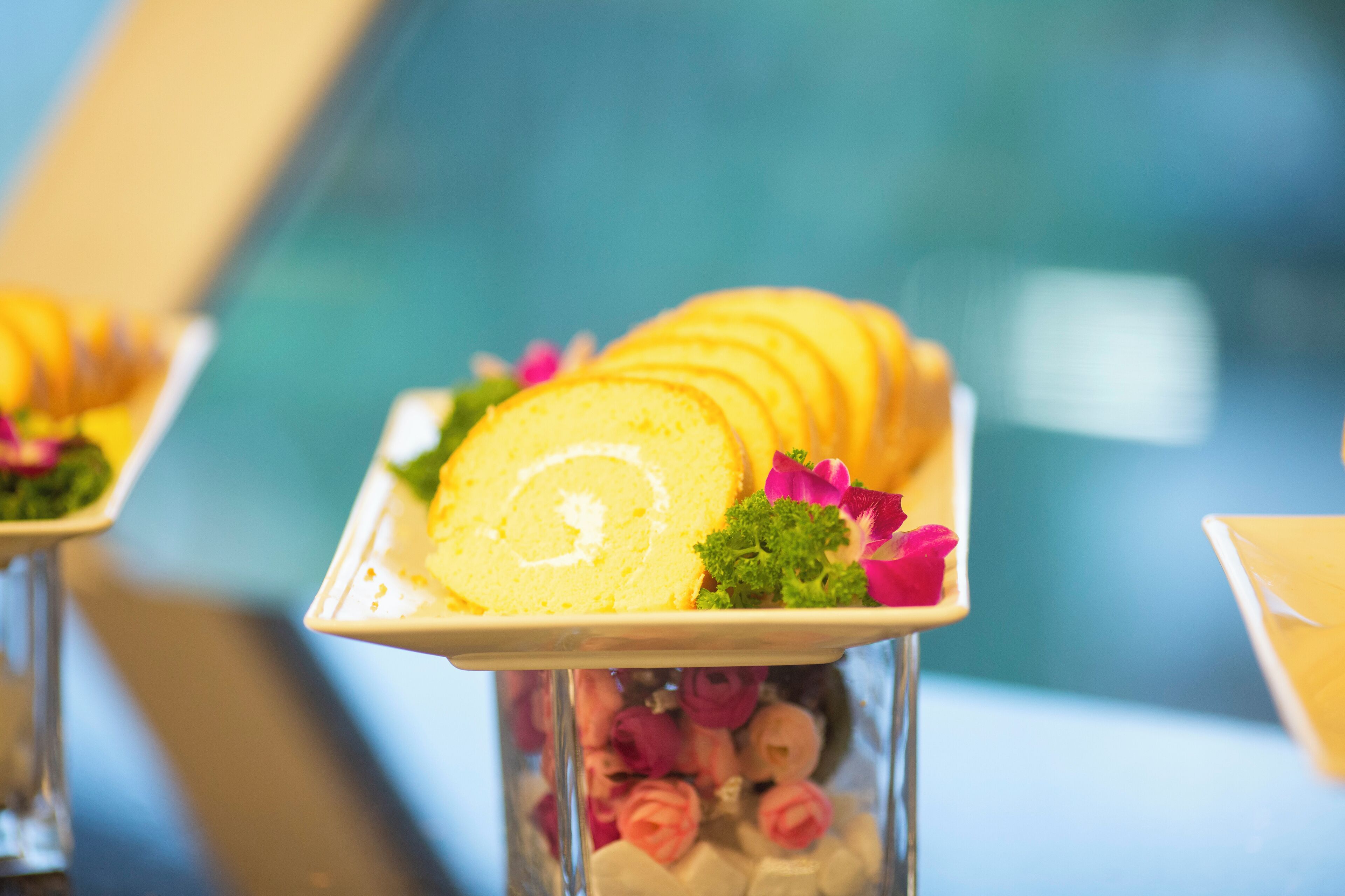 Un plateau de desserts avec un gâteau roulé, décoré de feuilles vertes et de fleurs roses, présenté sur une assiette blanche.