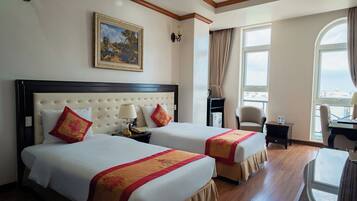 A hotel room with two beds, a desk, a chair, a window with curtains, and a painting on the wall.