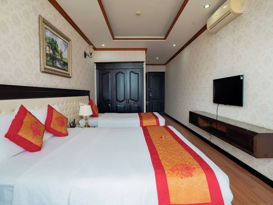 A hotel room with two beds, a TV, a wardrobe, and a painting on the wall.
