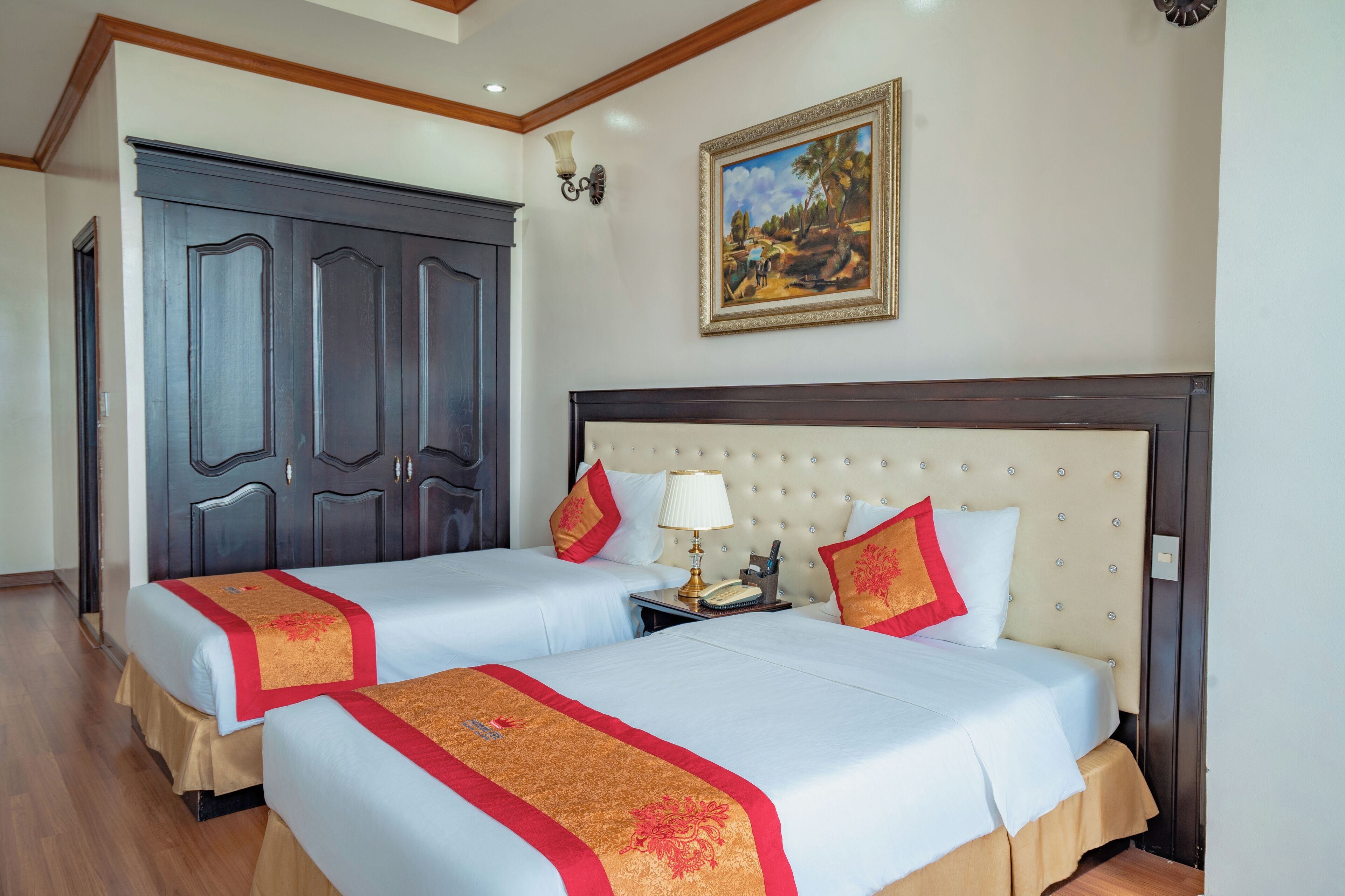 Habitación de hotel con dos camas, un armario grande, un cuadro en la pared y una mesita de noche con lámpara.