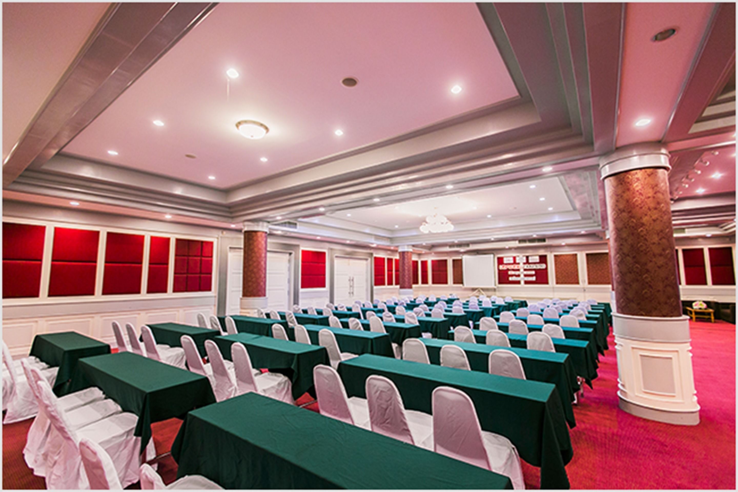 A conference room with rows of tables and chairs, a red carpet, and a pillar.