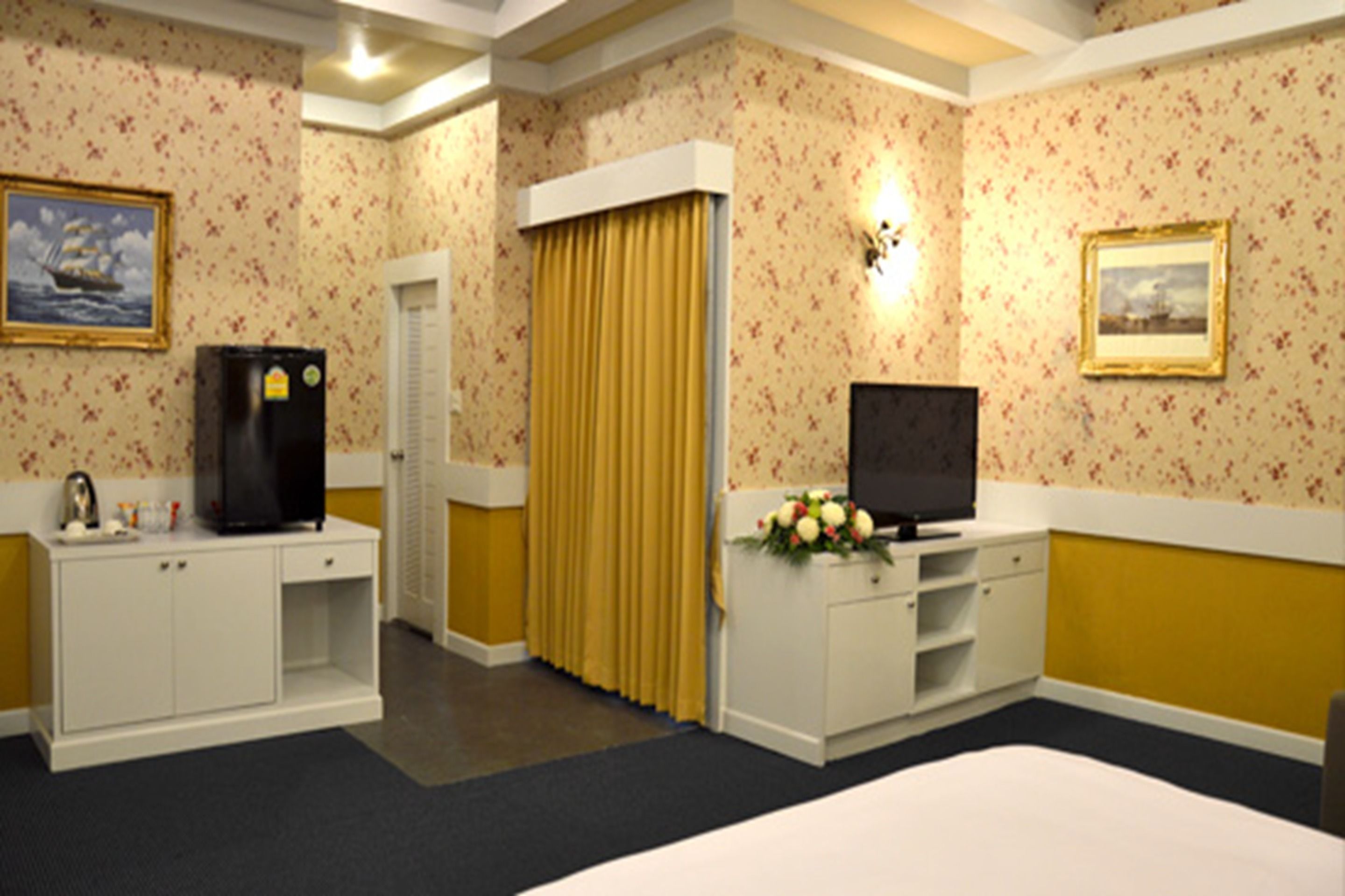 A hotel room with a bed, a TV, a minibar, a desk, and a door with curtains.
