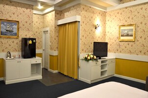 A hotel room with a bed, a TV, a minibar, a desk, and a door with curtains.