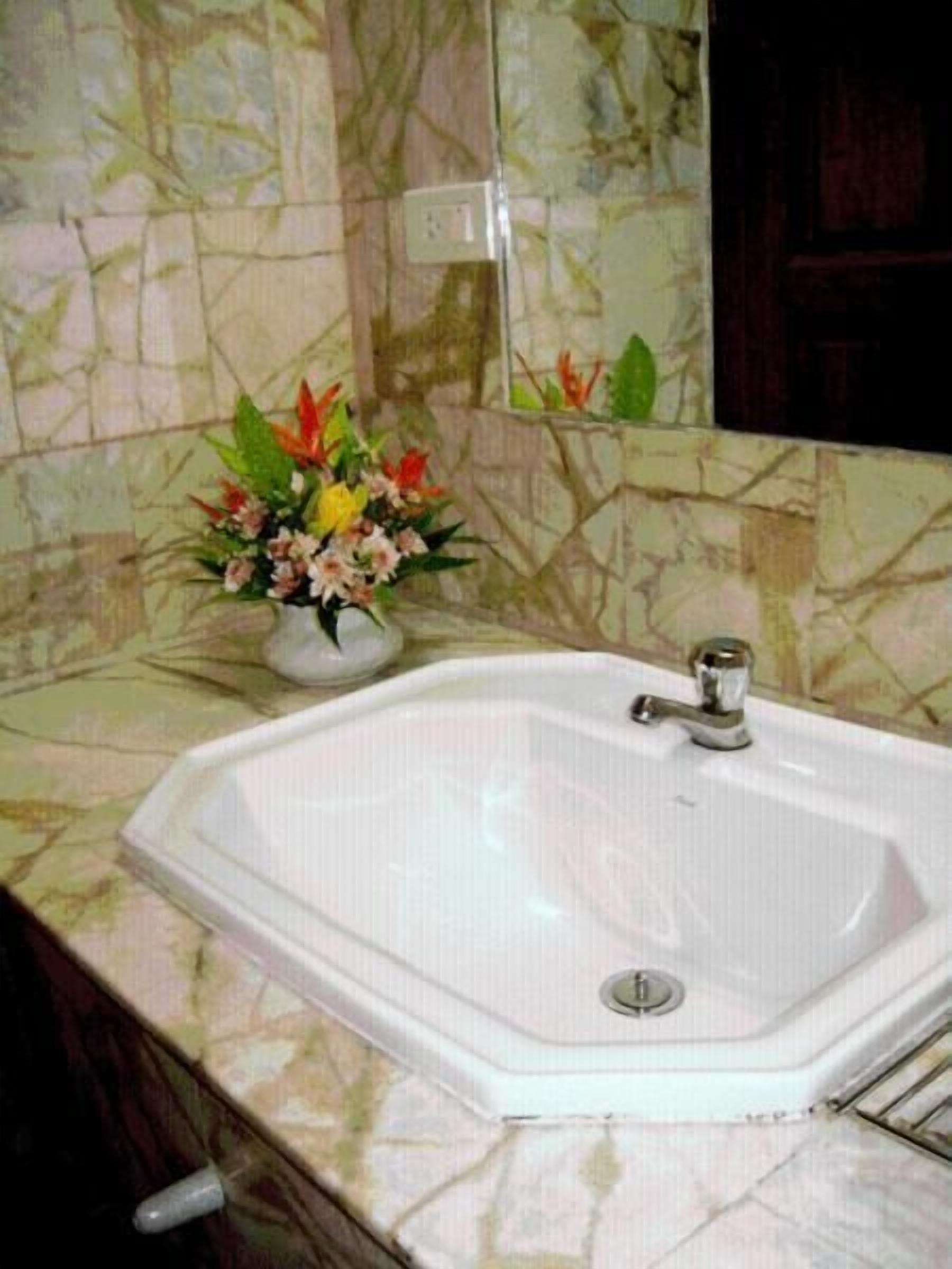 A bathroom with a white sink, a mirror, and a floral arrangement on the counter.
