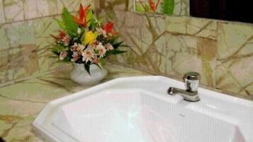 A bathroom with a white sink, a mirror, and a floral arrangement on the counter.