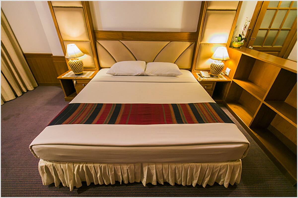 A hotel room with a large bed, two bedside tables with lamps, a headboard, and a carpeted floor.