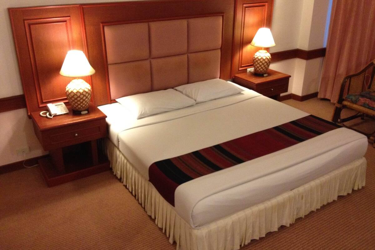 A hotel room with a large bed, two bedside tables with lamps, a telephone, and a chair.