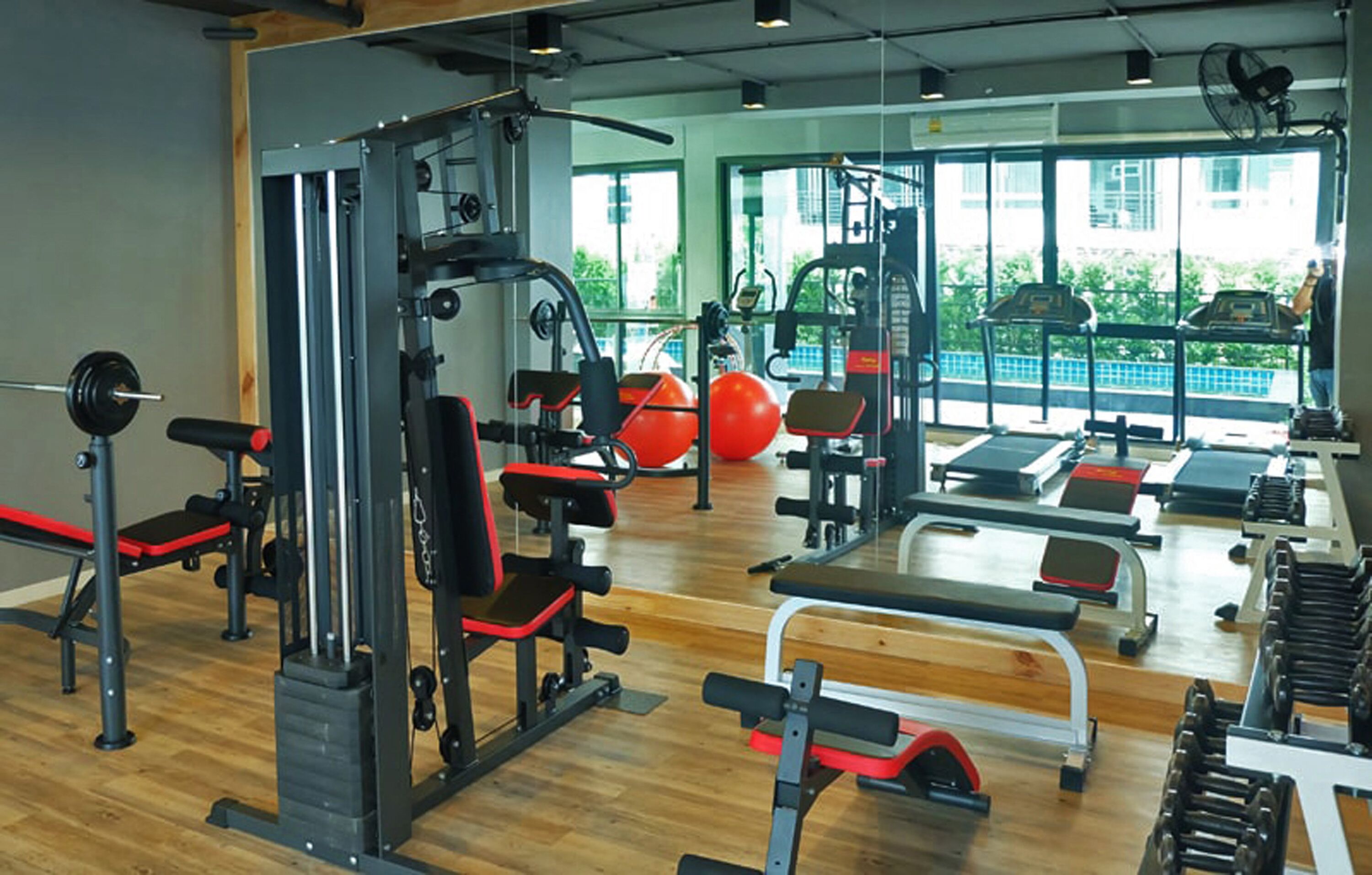 A gym with various exercise equipment, large windows, and a view of greenery outside.