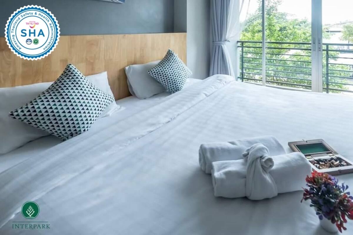 A neatly made bed with white linens, two patterned pillows, a set of towels, a tablet, and a small bouquet of flowers.