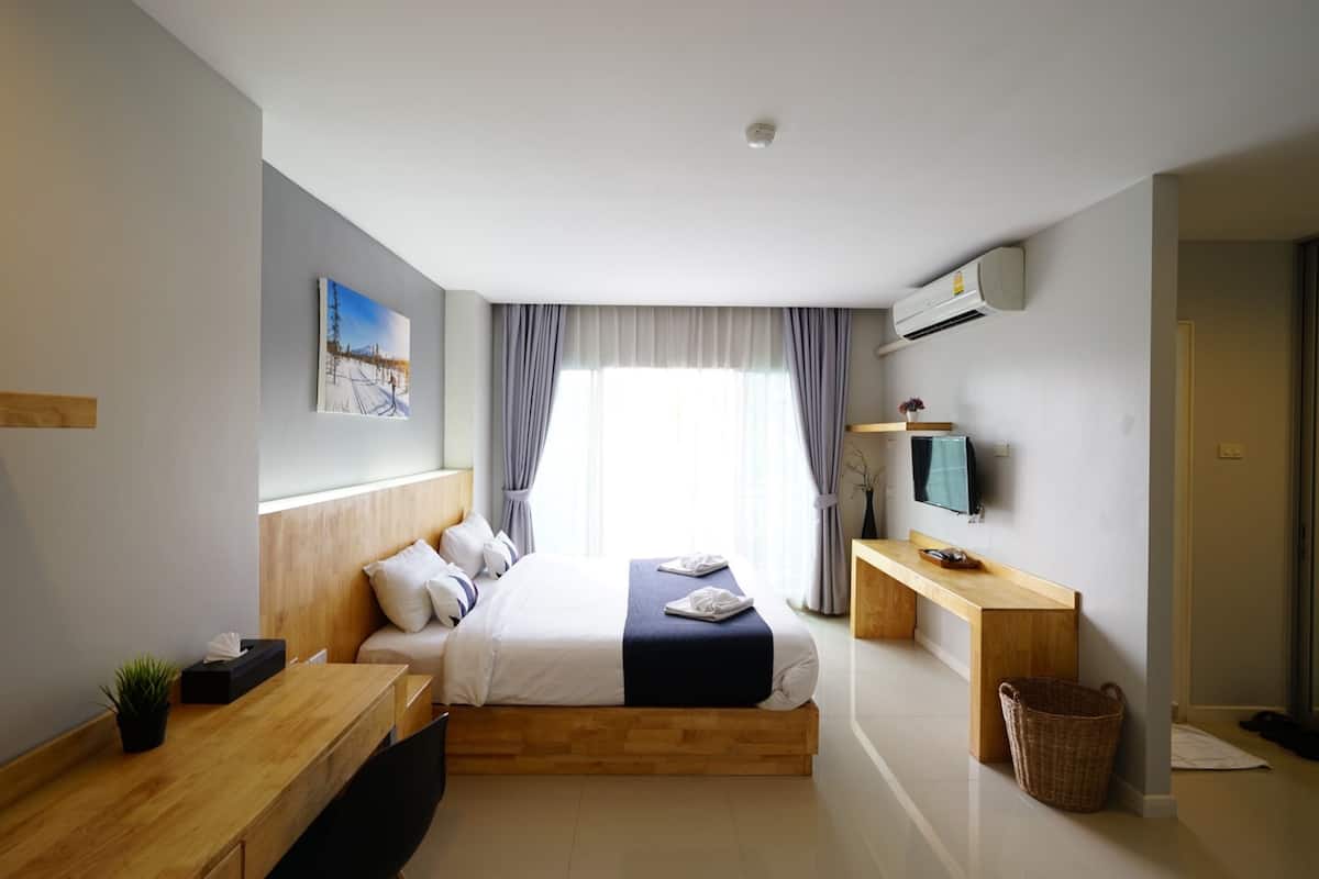 A modern hotel room with a wooden bed, a desk, a television, and a window with curtains.