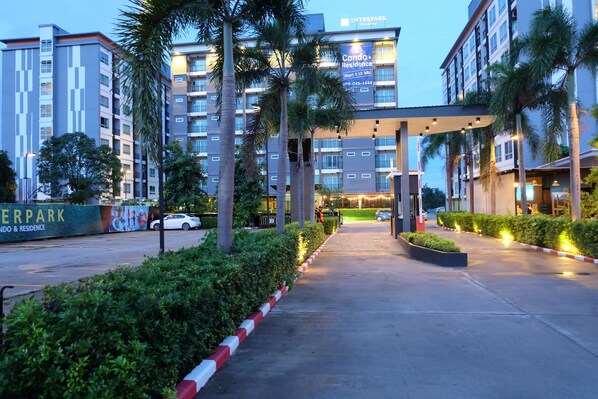 A modern residential building with a covered walkway, palm trees, and a sign for Interpark Condos & Residences. - Interpark Hotel & Residence Eastern Seaboard Rayong (Pluak Daeng)