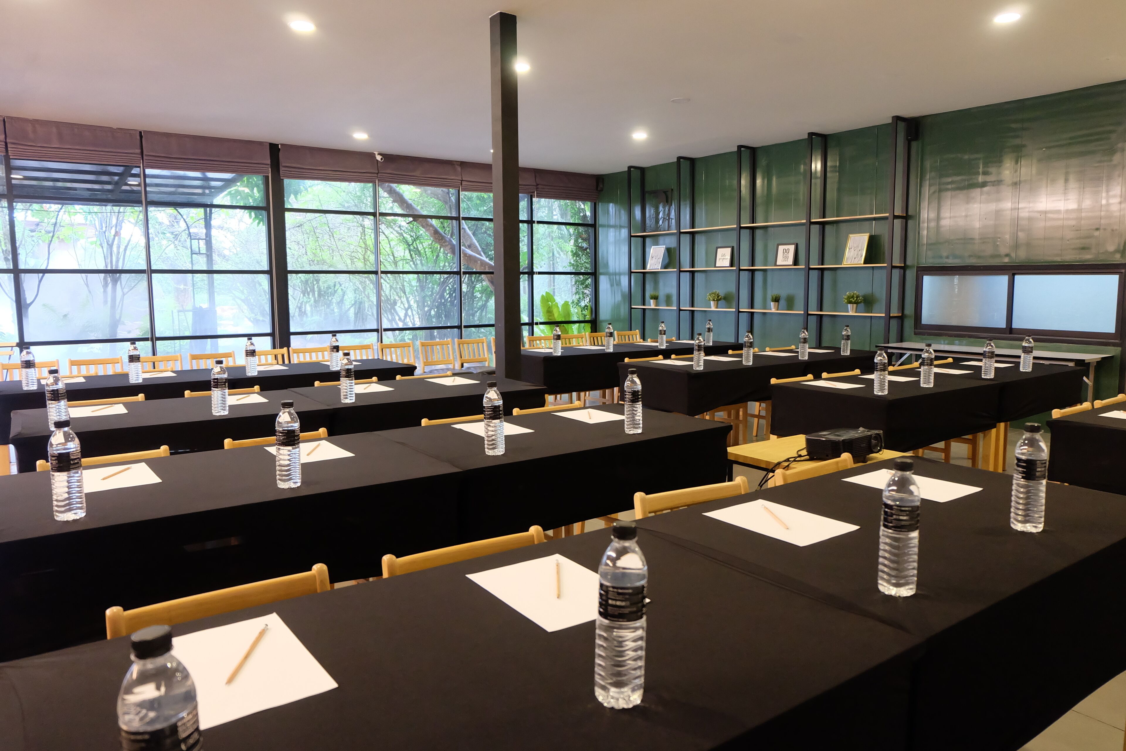 Ein Konferenzraum mit langen Tischen, Stühlen, Wasserflaschen und einem großen Fenster mit Blick auf Bäume.