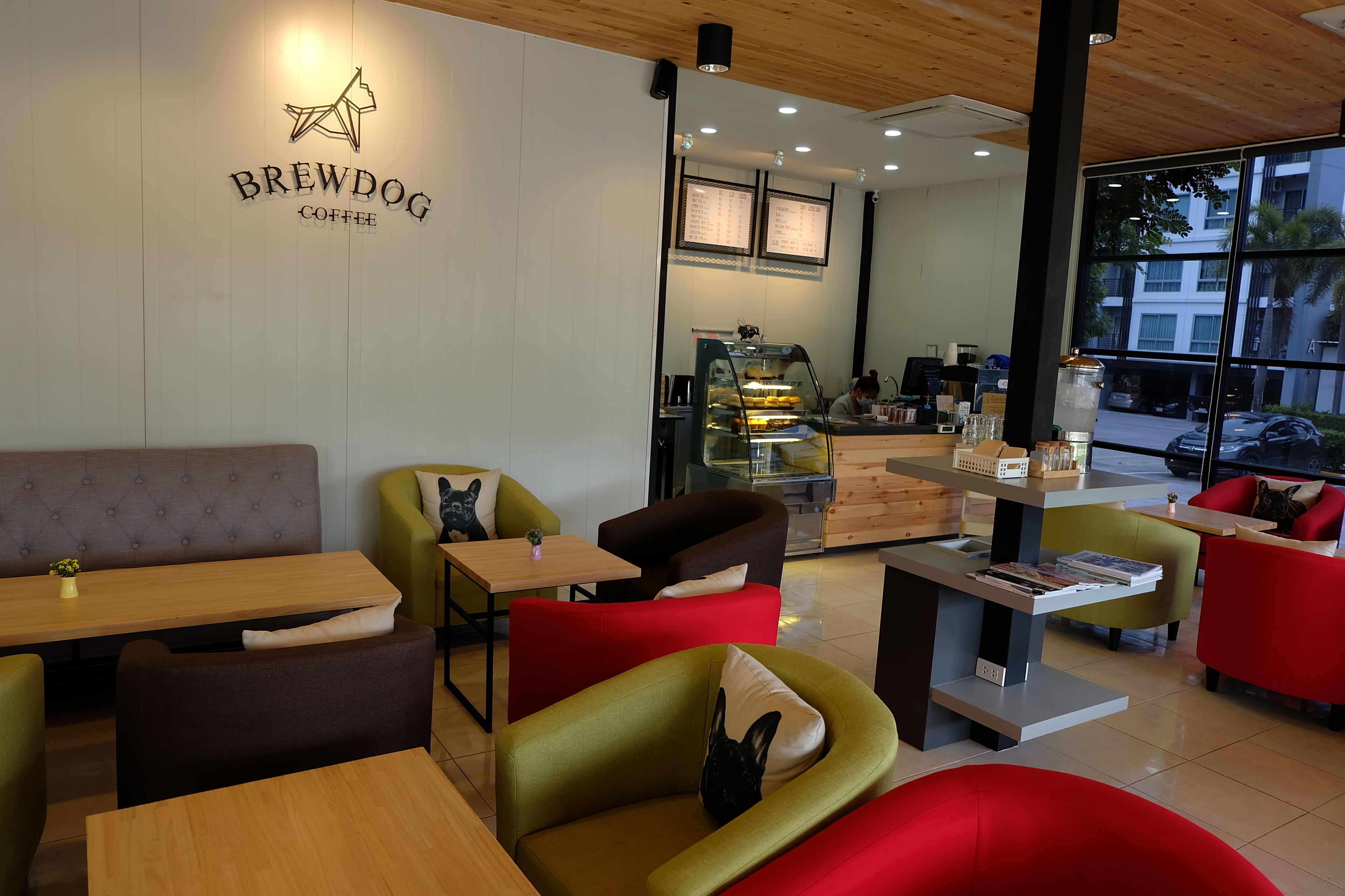 Interior de una cafetería con disposición de mesas, una barra y un tablero de menú.