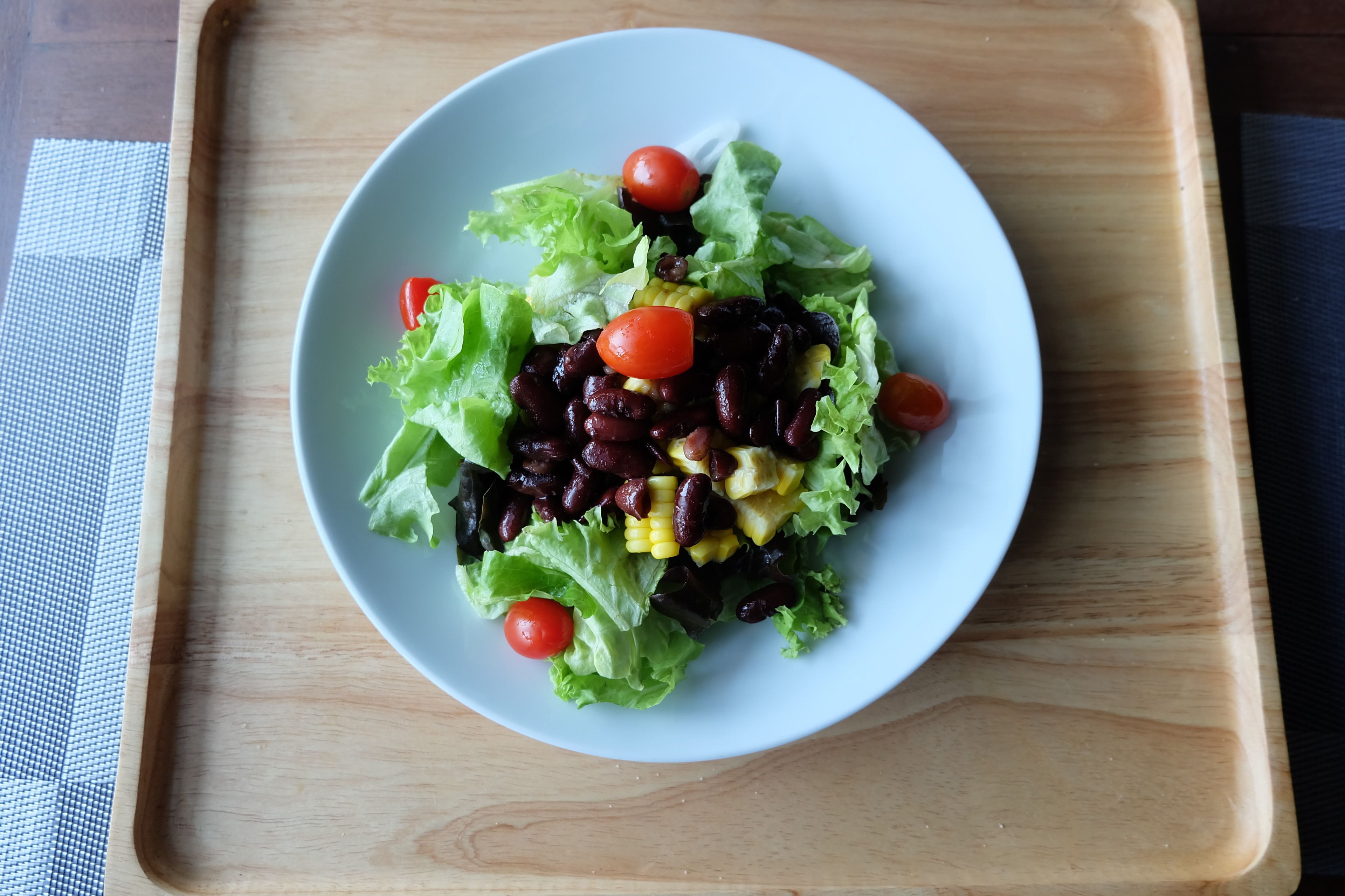 A plate of salad with lettuce, cherry tomatoes, black beans, corn, and yellow peppers on a wooden tray.