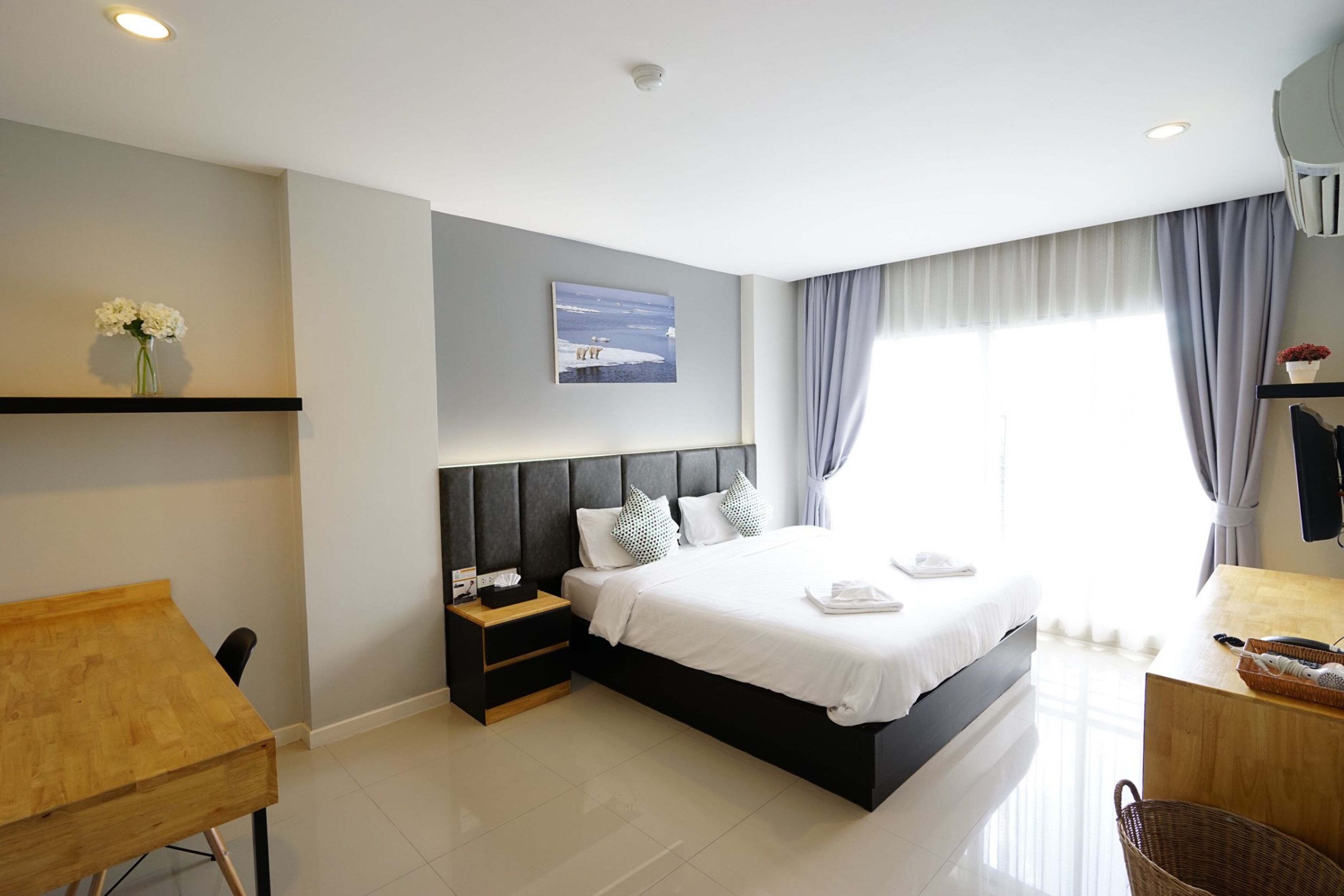 A modern hotel room with a large bed, bedside tables, a desk, and a view of the sea through the window.