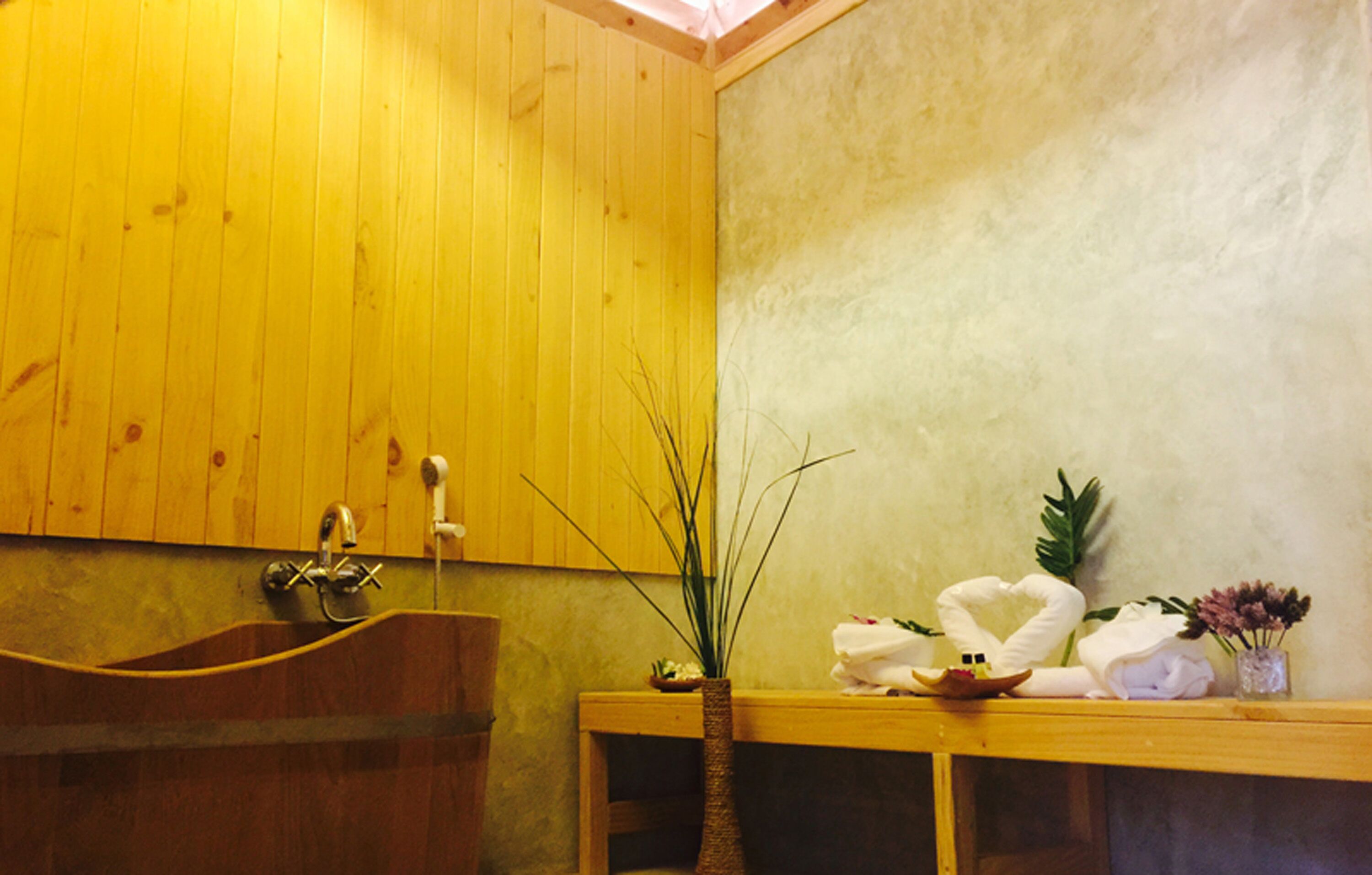 A wooden interior with a bathtub, a wooden bench, and a vase with plants.