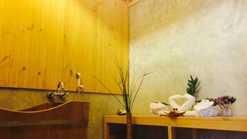A wooden interior with a bathtub, a wooden bench, and a vase with plants.