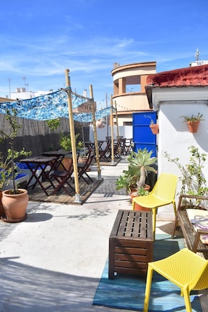 An outdoor patio area with wooden furniture, potted plants, and a blue tarp. - Casa Al Sur Terraza Hostel (Málaga)