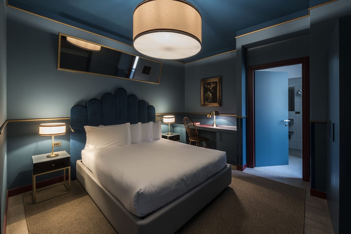A modern hotel room with a large bed, bedside lamps, a desk, and a mirror.