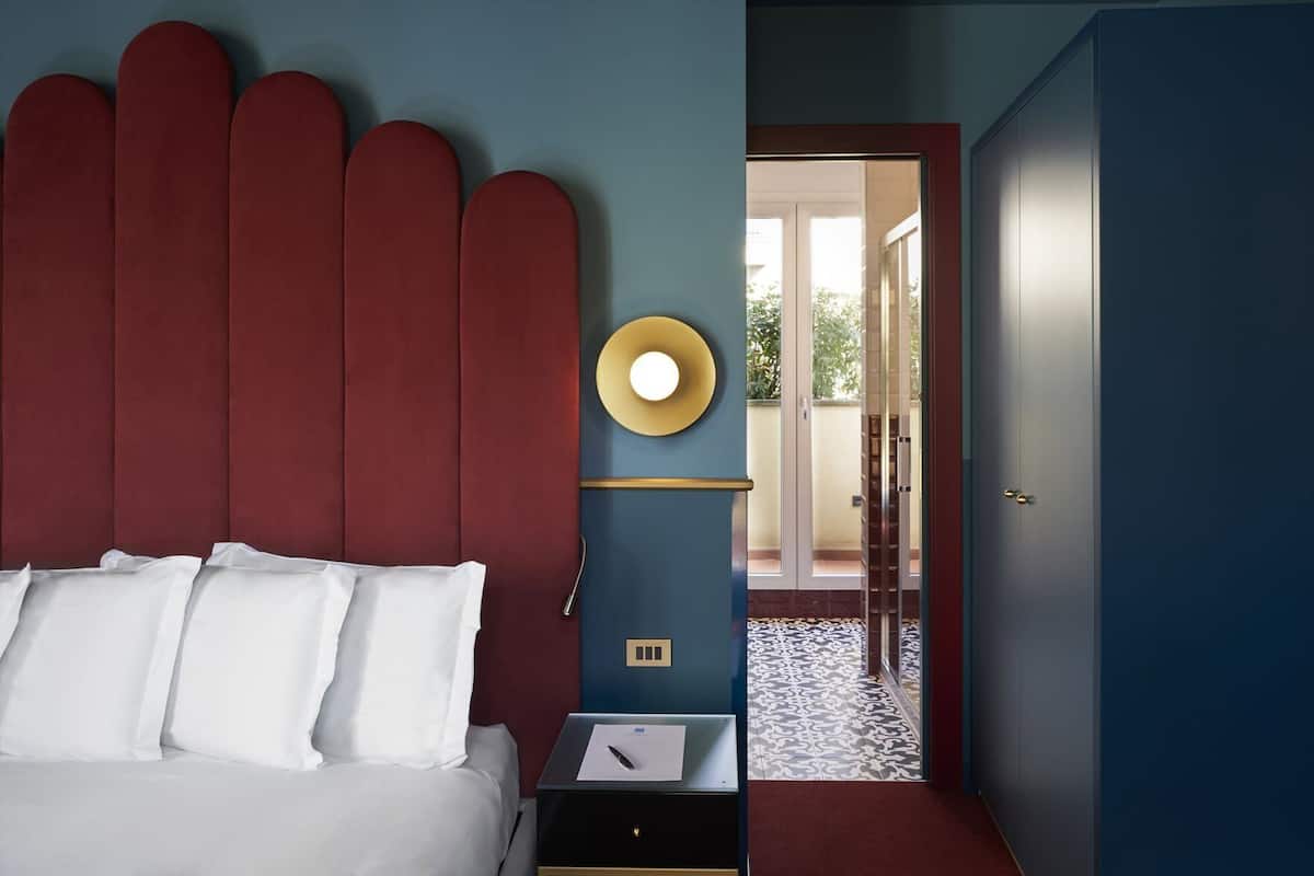 A bedroom with a bed, bedside table, and a view of the outside.