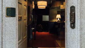 Een gebogen doorgang die uitkomt in een hotel lobby met een rode loper, een receptiebalie en een lamp.