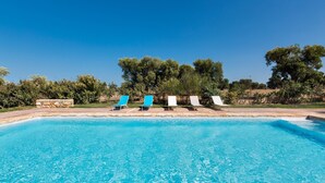 Une piscine d’un bleu éclatant, avec des chaises longues et un mur de pierre en arrière-plan.