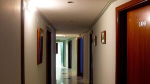 Un pasillo de hotel con suelo de cuadros, puertas numeradas 106 y cuadros enmarcados en las paredes.