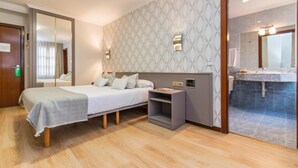 Una habitación de hotel moderna con una cama, una mesita de noche y un baño visible a través de una puerta de cristal.