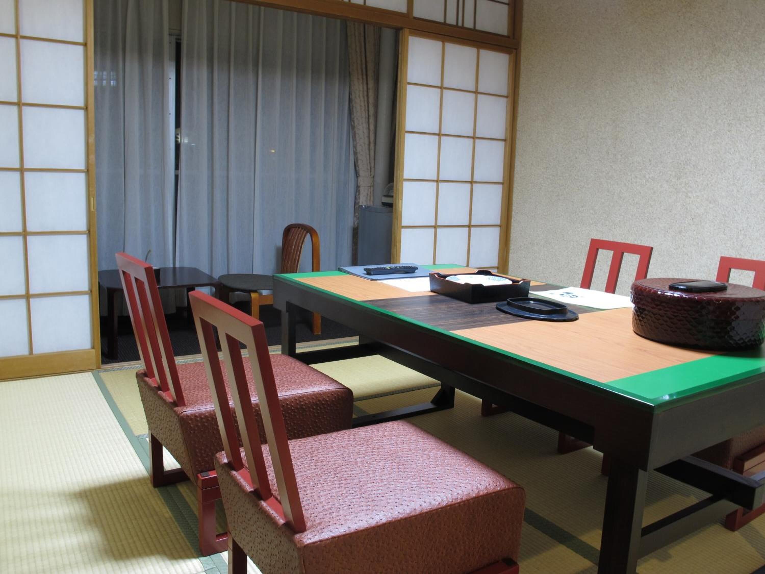 Ein traditioneller japanischer Raum mit Tatami-Böden, einem niedrigen Tisch und roten Stühlen.