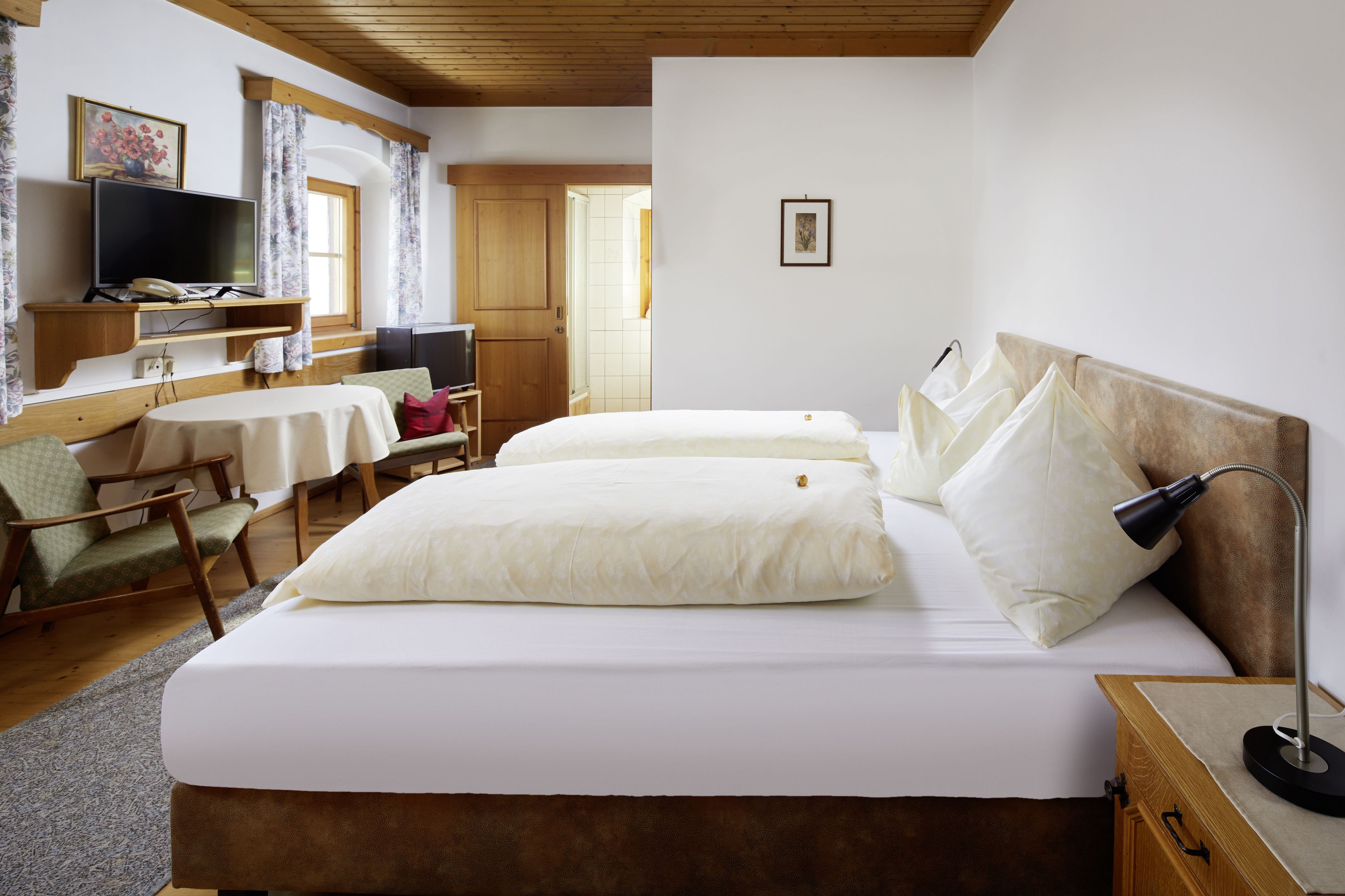 A hotel room with two beds, a TV, a desk with a chair, and a wooden ceiling.
