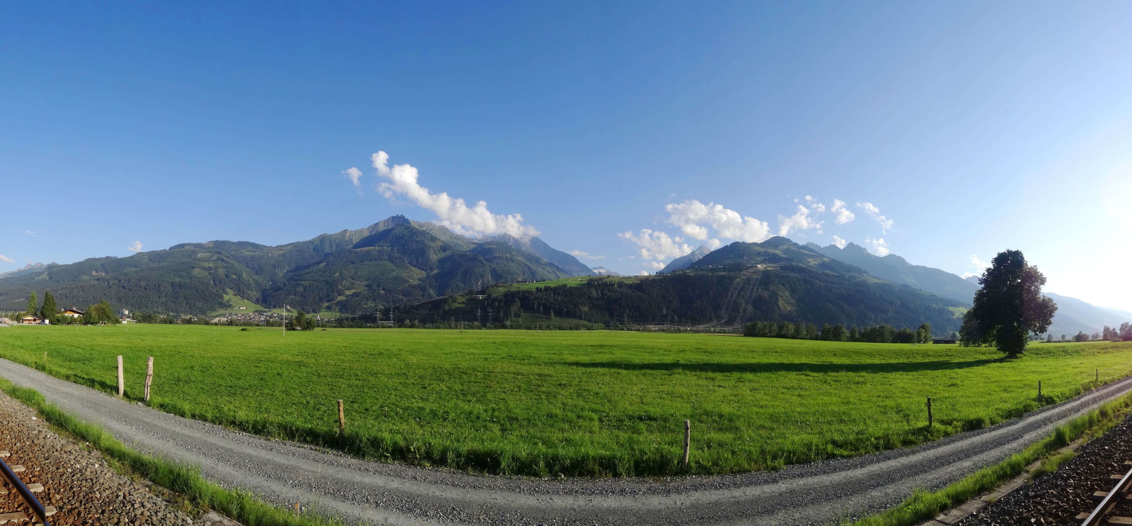 A rural landscape with a road, green fields, and mountains in the background.