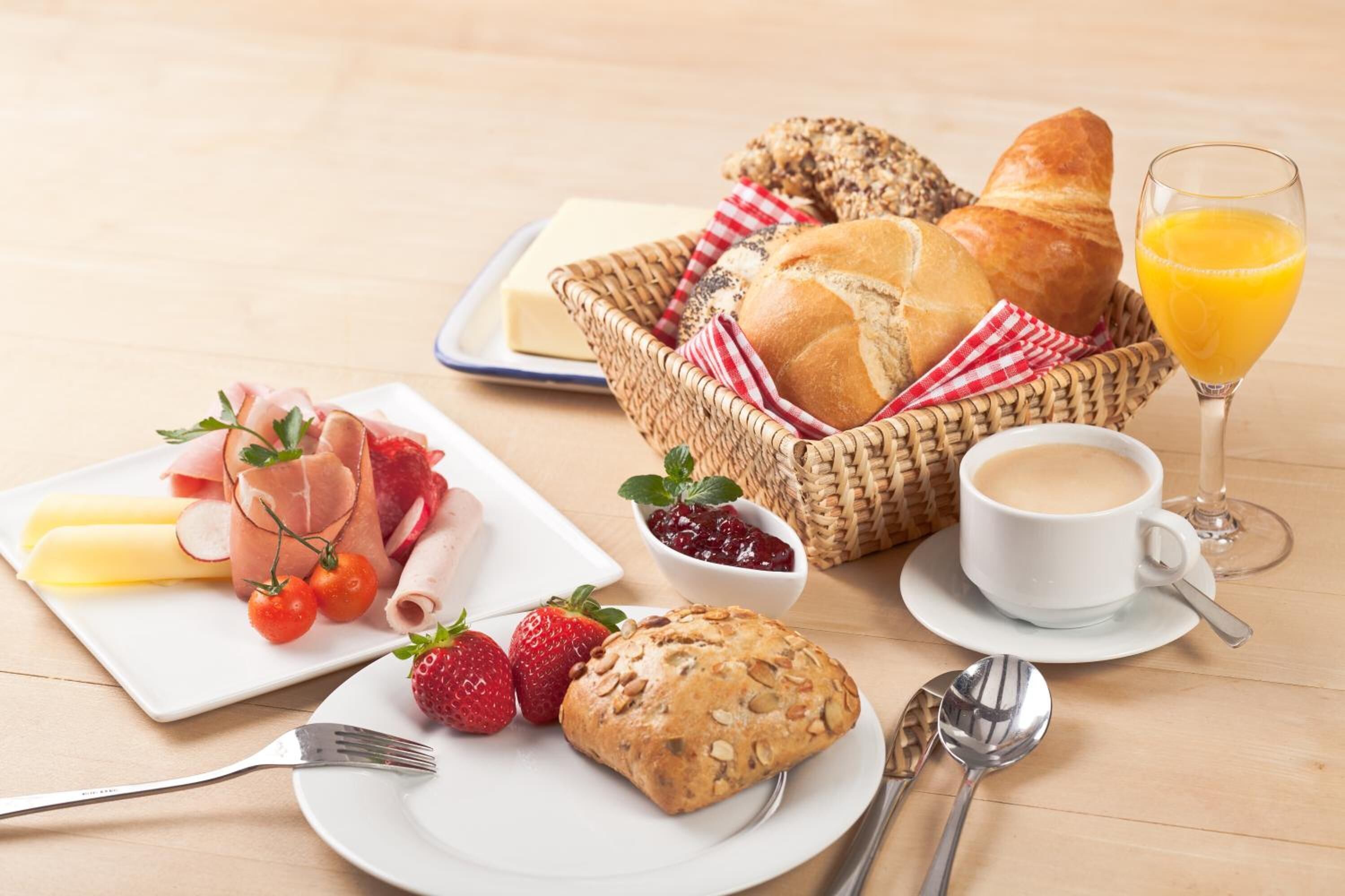 A breakfast setting with bread, pastries, fruit, cheese, and a glass of orange juice.
