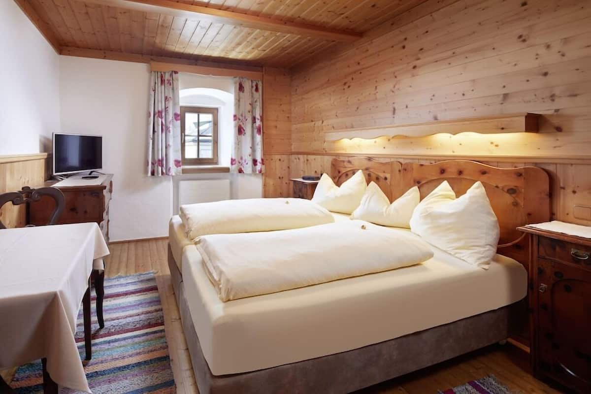 Una habitación de madera con dos camas, una mesa, un televisor y una ventana con cortinas.