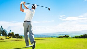 Une personne jouant au golf sur un terrain bien entretenu, sous un ciel dégagé, avec un paysage lointain.