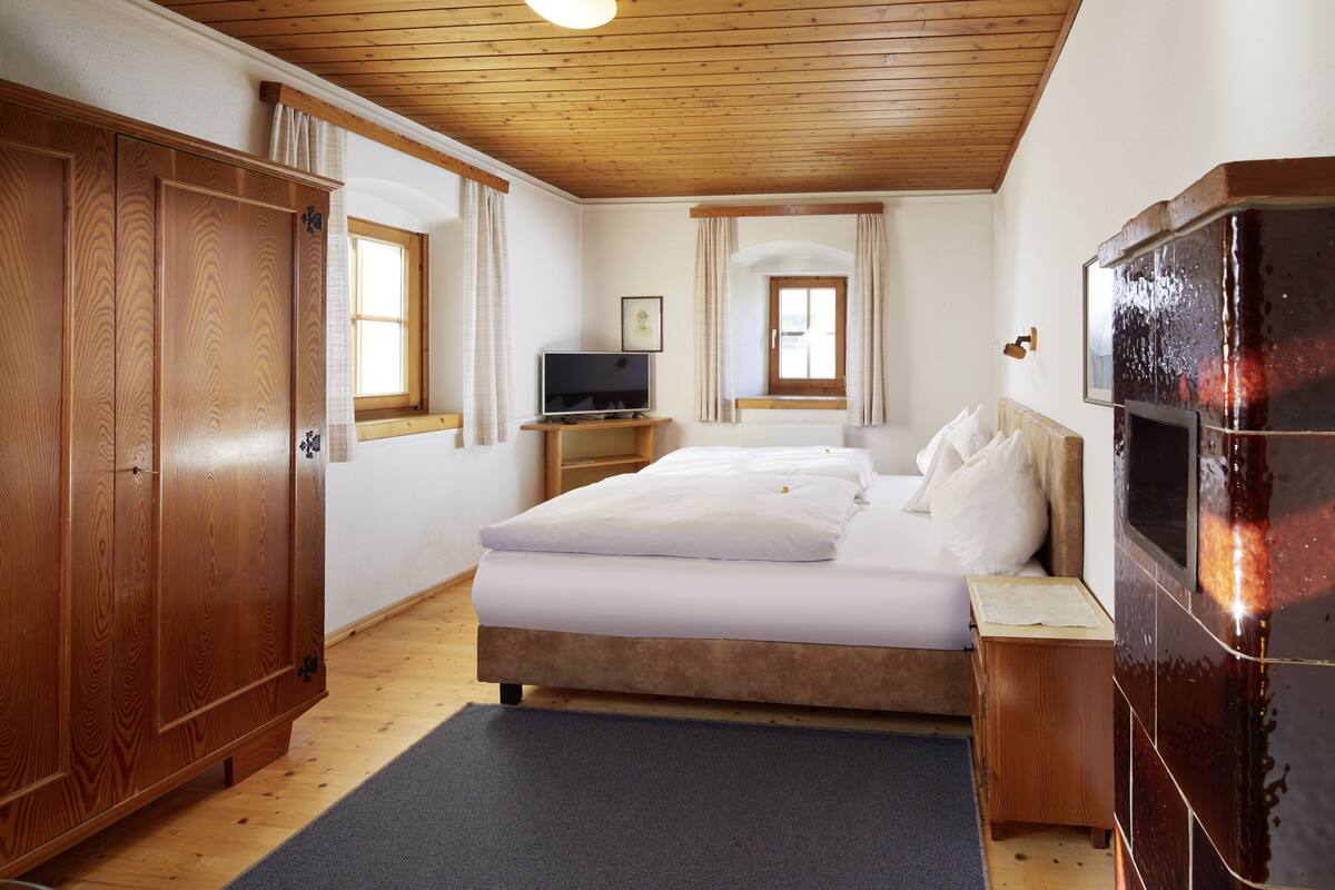 Un dormitorio con techo de madera, una cama con ropa blanca, un televisor sobre un soporte de madera y una chimenea.
