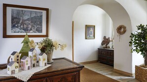 Une pièce avec une commode en bois, un petit sapin de Noël et un vase de fleurs. Il y a un tableau encadré au mur et une couronne accrochée à la porte.