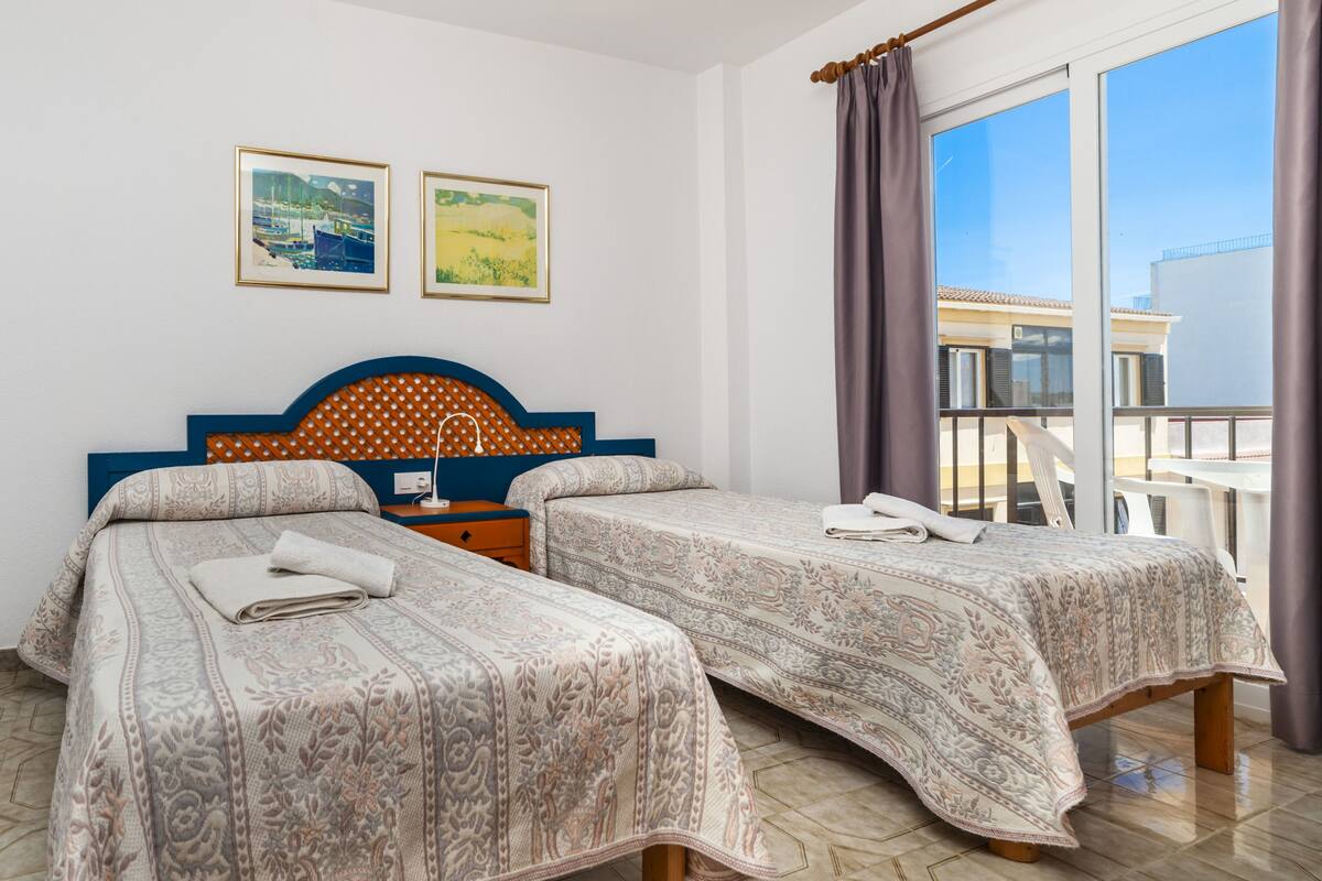 Une chambre d’hôtel avec deux lits, une tête de lit en bois, une table de chevet et un balcon avec vue.
