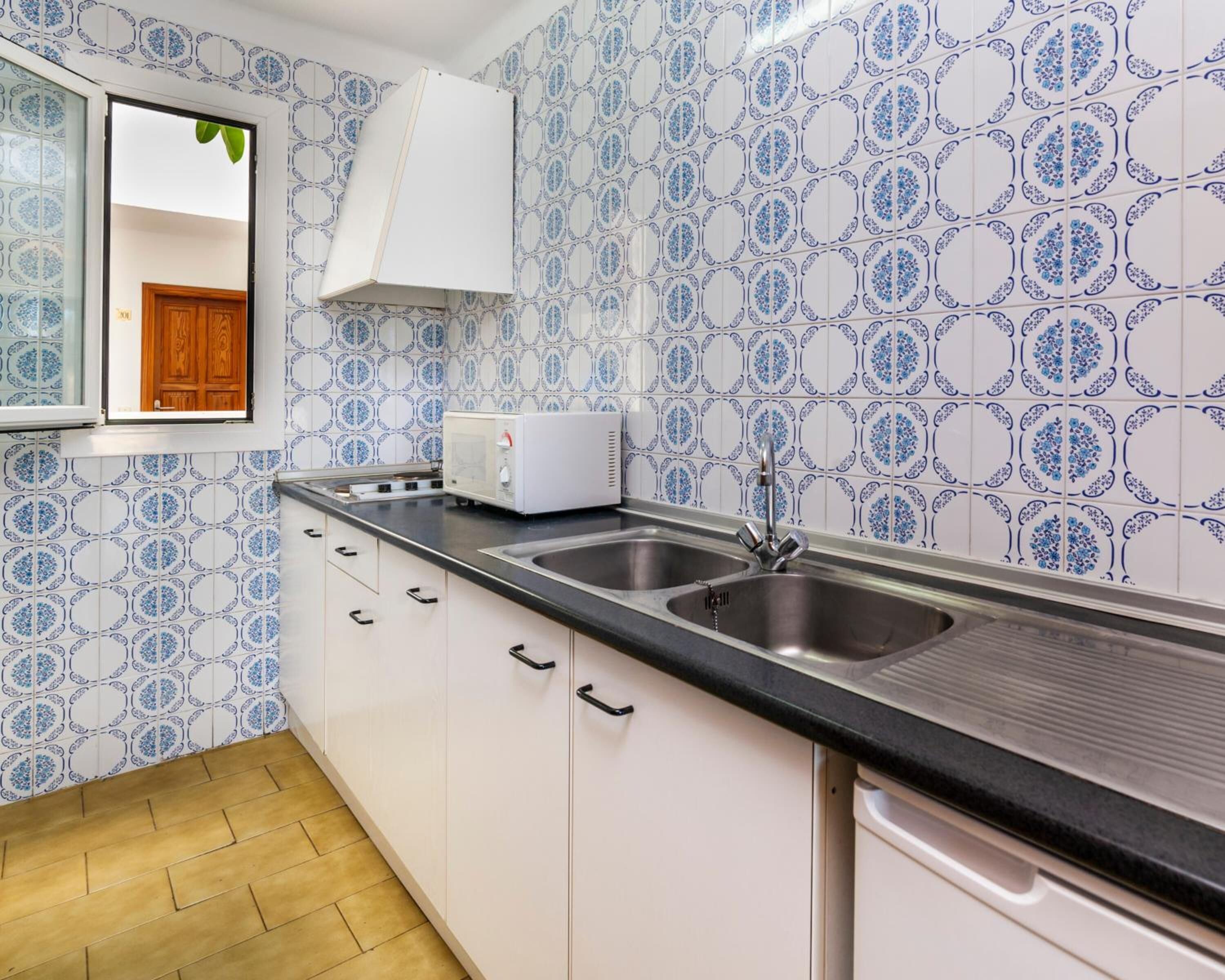 A kitchen with white cabinets, a black countertop, and a sink. The backsplash has a blue and white pattern.