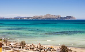Una playa con aguas turquesas cristalinas, sombrillas y una montaña al fondo.