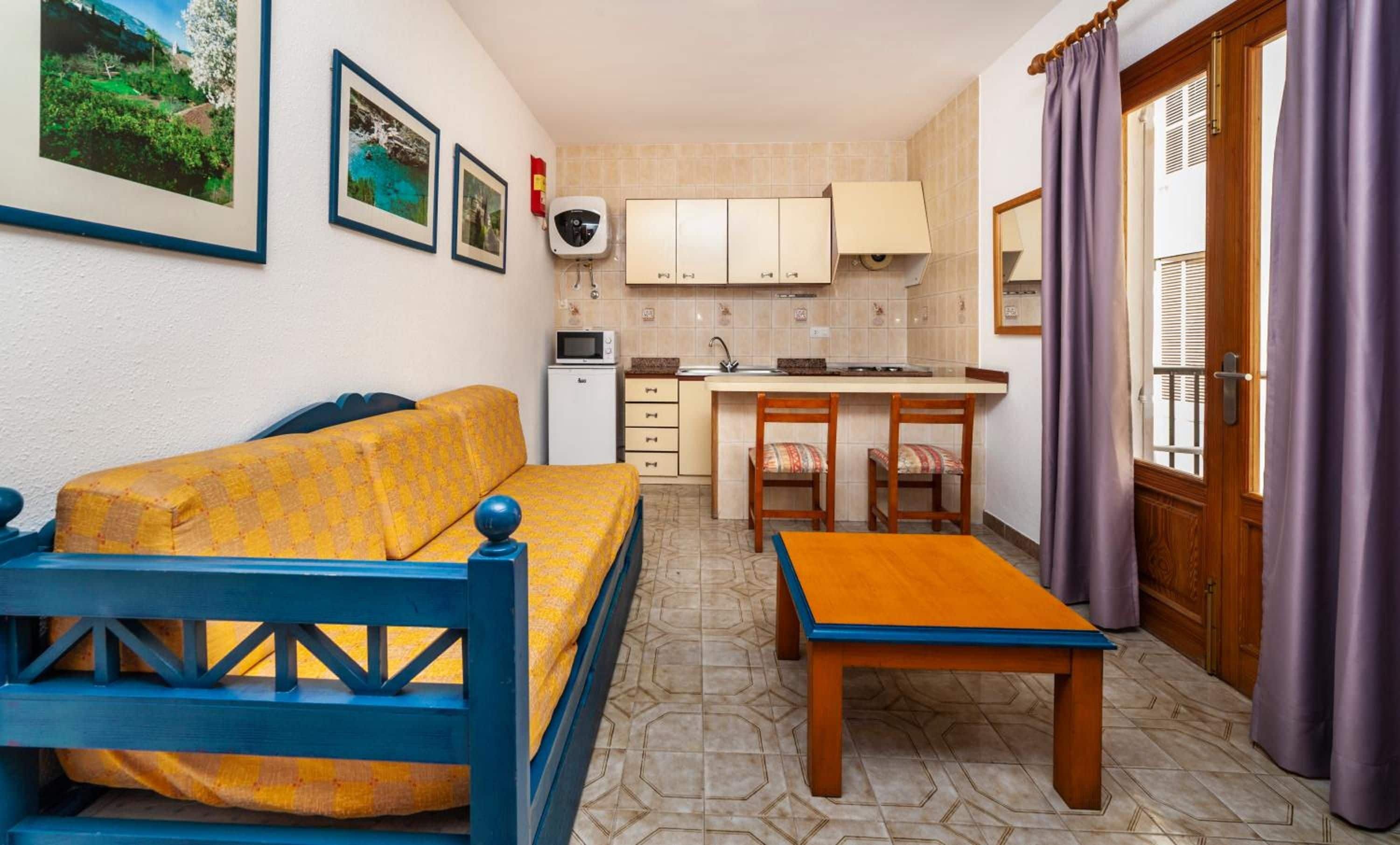 A compact living space with a sofa, a small dining table, a kitchenette, and a window with curtains.