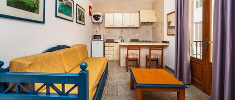 A compact living space with a sofa, a small dining table, a kitchenette, and a window with curtains.