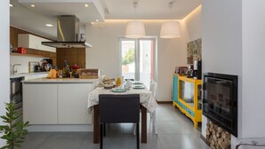 A modern kitchen with a dining area, featuring a central island, a built-in oven, and a colorful cabinet. - Downtown Alegria B&B (Tavira)