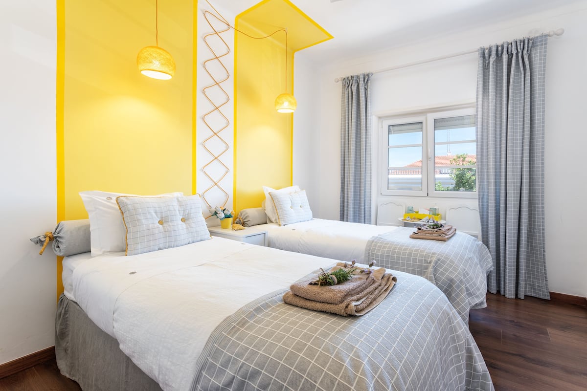 Une chambre d’hôtel avec deux lits, une fenêtre avec des rideaux et un mur d’accent jaune.