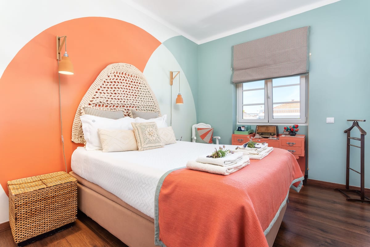 Une chambre à coucher bien rangée, avec un lit, une table de chevet, une lampe et une fenêtre donnant sur un beau paysage.