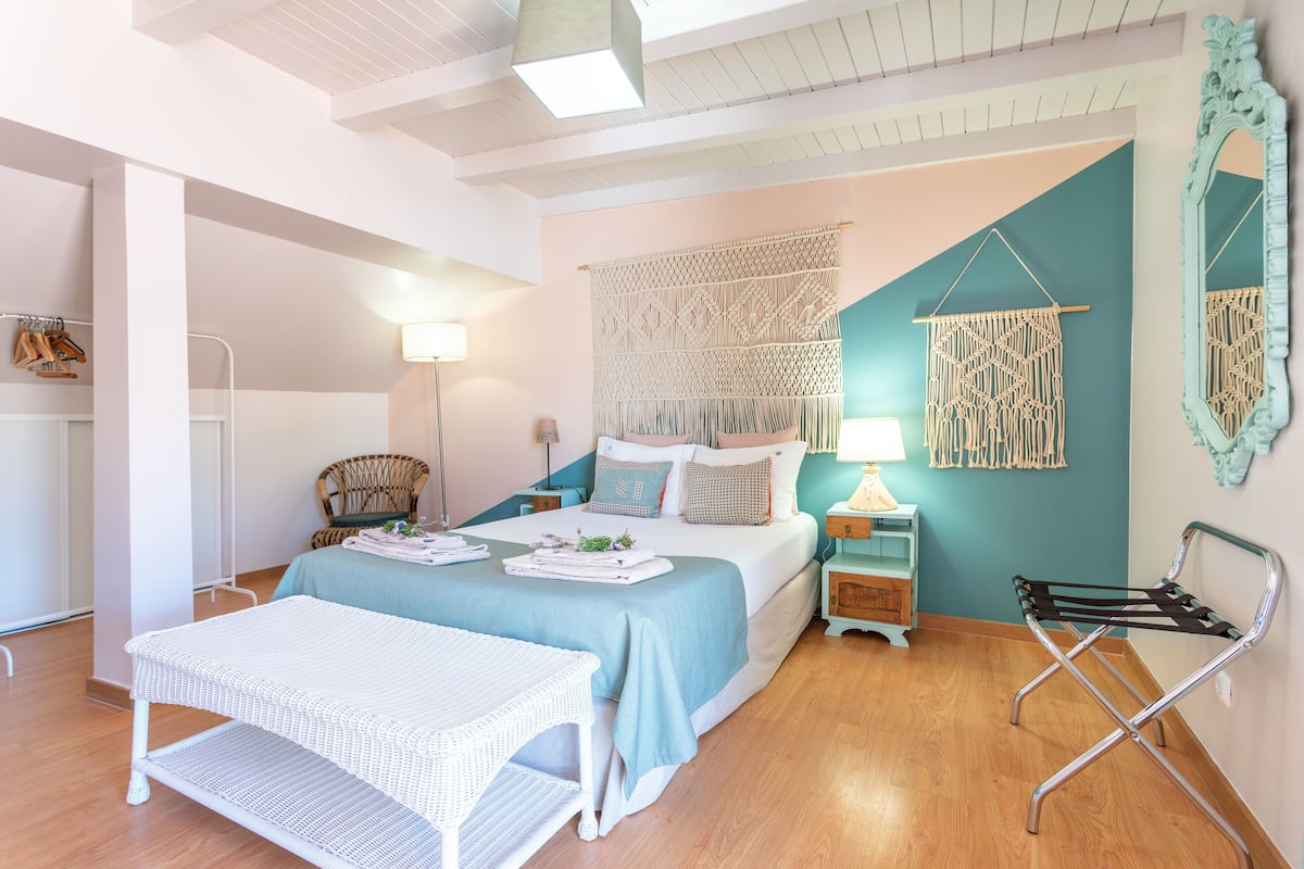 Une chambre à coucher bien rangée, avec un lit, des tables de chevet, une chaise et une décoration murale en macramé.