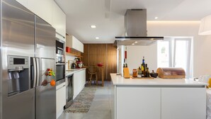 A modern kitchen with stainless steel appliances, a central island, and a wooden accent wall. - Downtown Alegria B&B (Tavira)