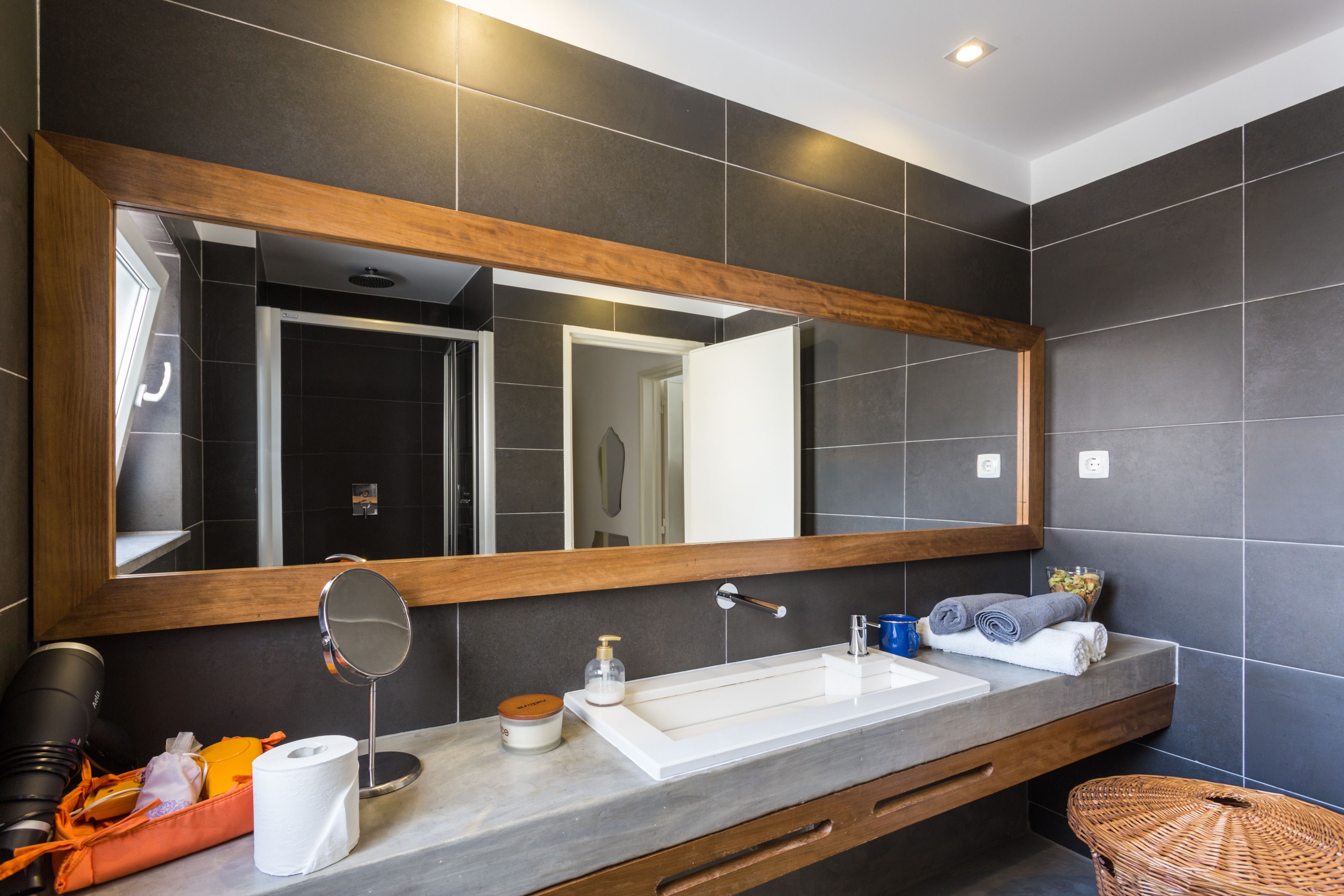 Une salle de bain moderne avec un grand miroir, un lavabo blanc et un meuble-lavabo en bois.