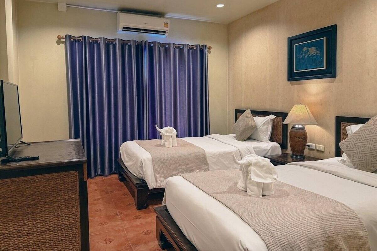 Een hotelkamer met twee bedden, een bureau, een airconditioner en een ingelijste foto aan de muur.