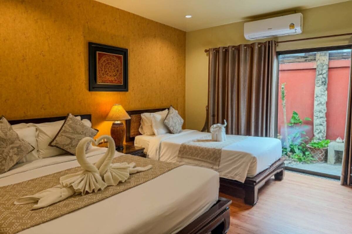 Een hotelkamer met twee bedden, een wandairconditioner, een ingelijst schilderij en uitzicht op een binnentuin door een glazen deur.
